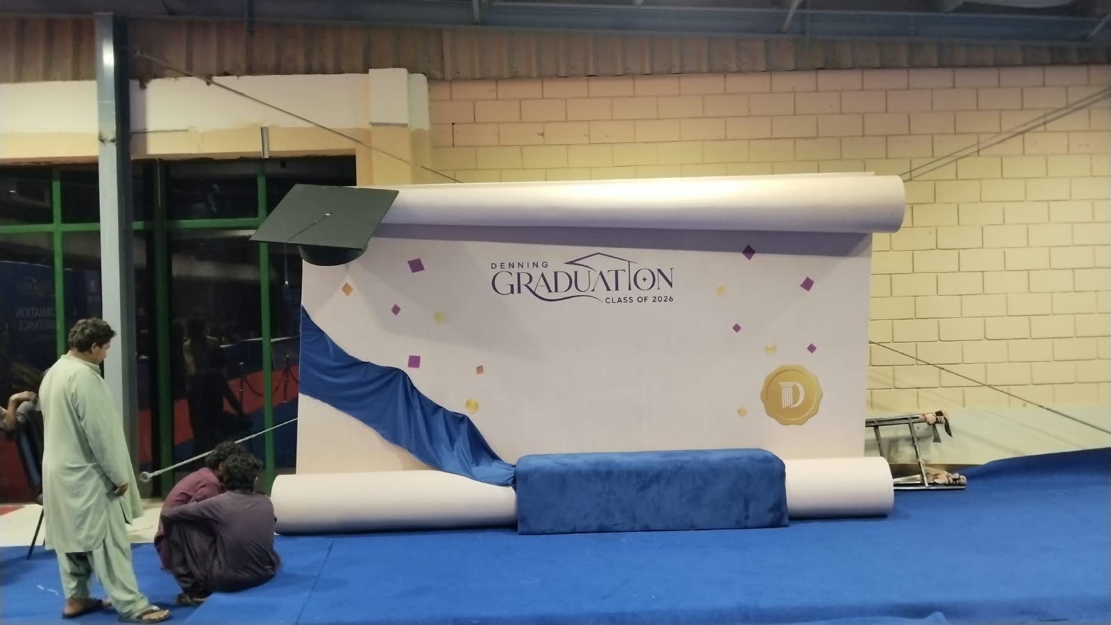 Large branded graduation-themed display stand being installed by the Booth Design Karachi team at Expo Centre Karachi for the Denning 5th Graduation Ceremony
